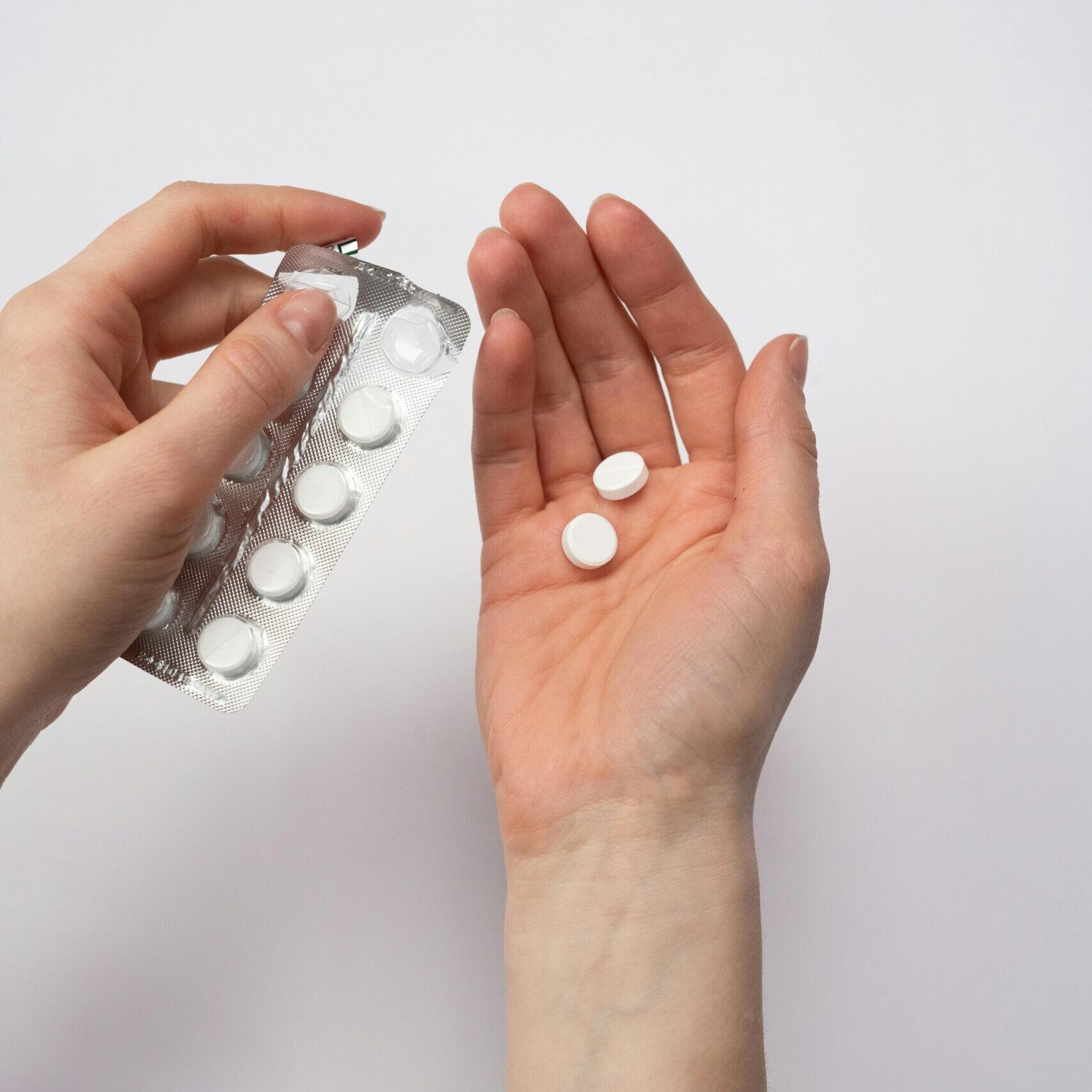 A person's hands holding white pills, symbolizing health and medication care.